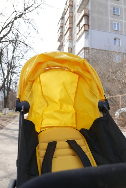 A vibrant yellow baby stroller is hit by sunlight on a city sidewalk with a tall building in the background.