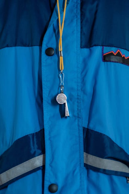 A close-up of a blue jacket featuring a whistle and lanyard, showcasing outdoor apparel.