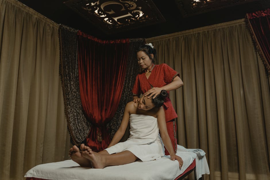 A masseuse in a red outfit provides a traditional massage to a client in a serene spa setting.