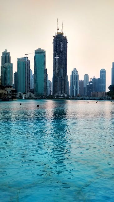 View of Dubai skyline with modern skyscrapers reflecting in waterfront at dusk.