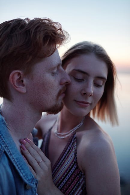 A serene moment of a couple embracing by the water at sunset, capturing love and connection.