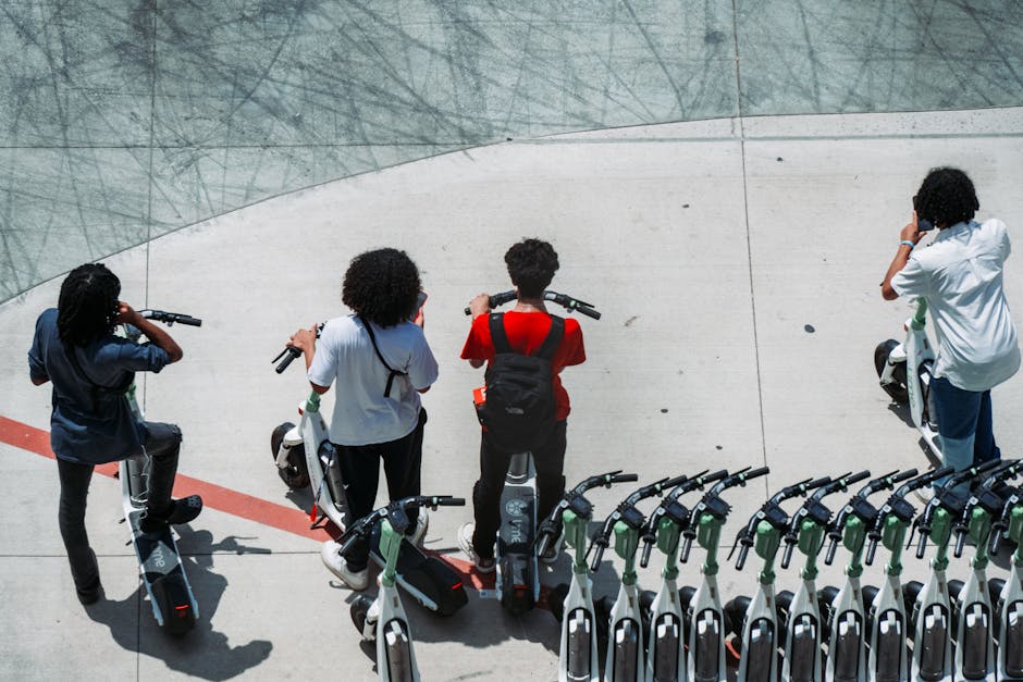 Group of young adults using electric scooters on a sunlit urban pavement.
