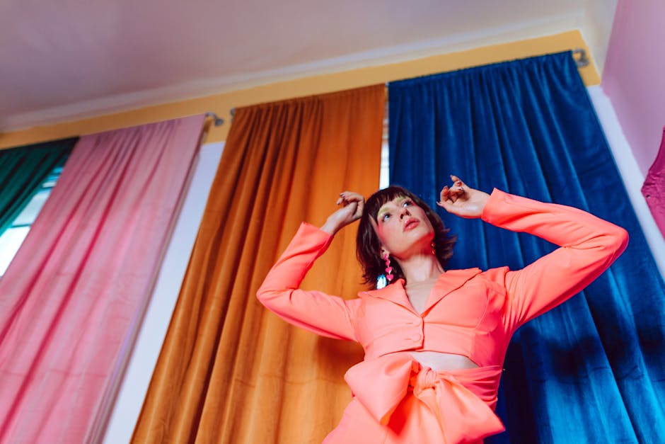 Stylish woman in a pink outfit posing indoors against colorful curtains.