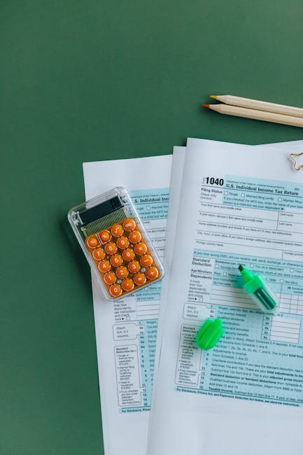 1040 tax forms with calculator, pencils, and markers on green surface.