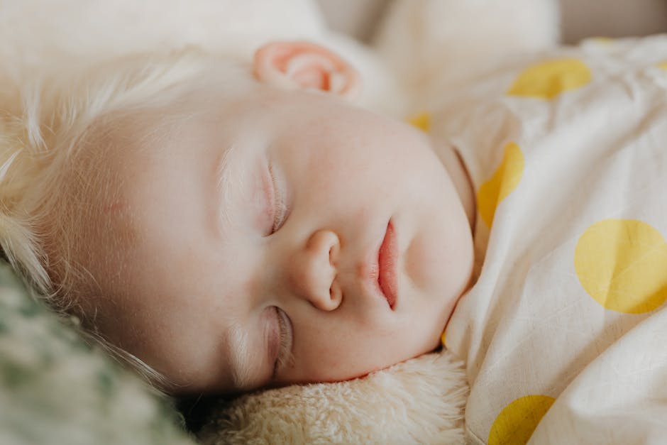 Close-up of a sleeping baby with white hair and a polka dot blanket. Tranquil and cute scene.