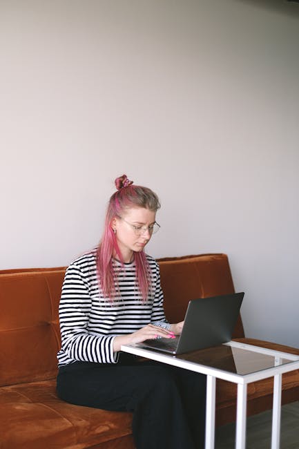 Young woman with pink hair working on a laptop at home, embodying the freelance lifestyle.