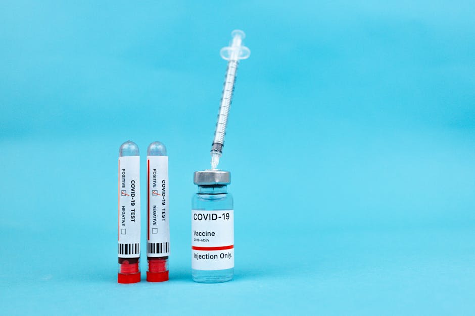 Vaccine vial and blood test tubes labeled COVID-19 on a blue surface, representing healthcare progress.