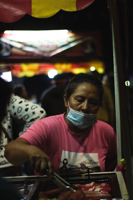 Woman wearing a face mask cooking at an outdoor street food market at night.