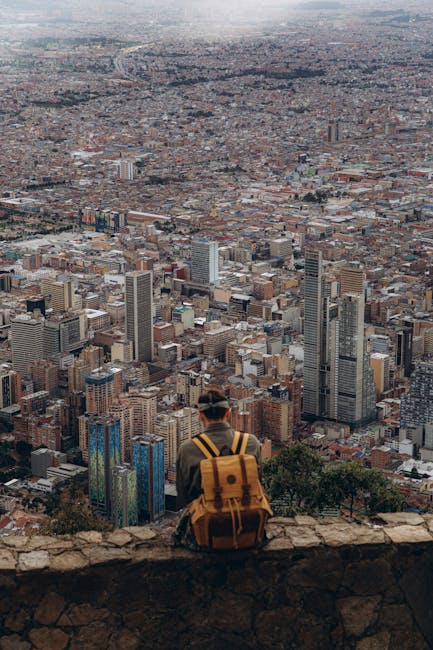 Person sits on cliff edge overlooking a vast cityscape, capturing the urban sprawl below.