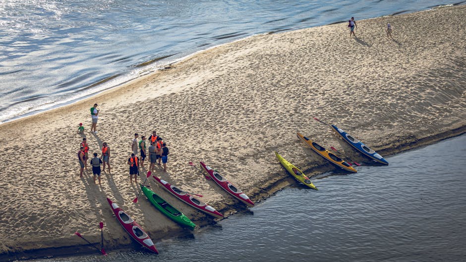 Aerial view of a group of people preparing kayaks on a sandy beach with vibrant colored boats.