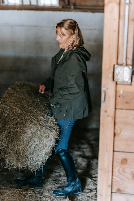 A woman in a stable carrying a hay bale, showcasing farm life and strength.