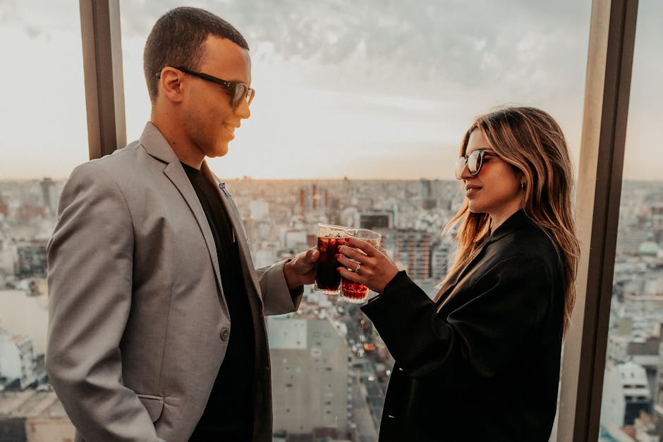Two adults toasting drinks on a rooftop in Buenos Aires during sunset, wearing fashionable outfits.