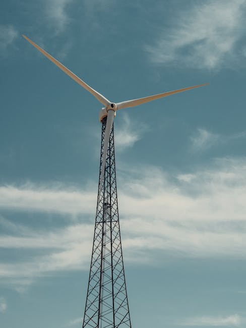 Low-angle view of a wind turbine against a cloudy blue sky, representing clean energy.