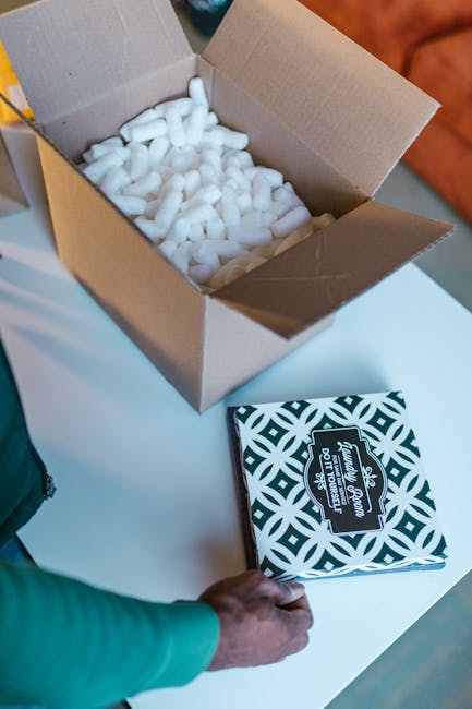 Open cardboard box with packing peanuts and hand placing patterned item.