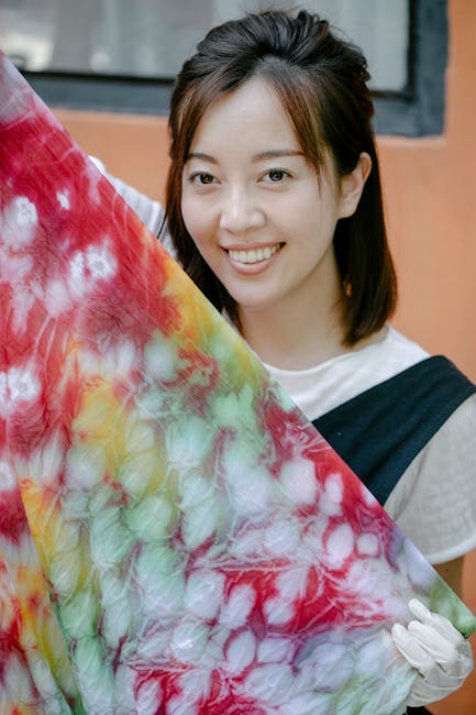 Asian woman smiling and holding a vibrant tie-dye fabric indoors.