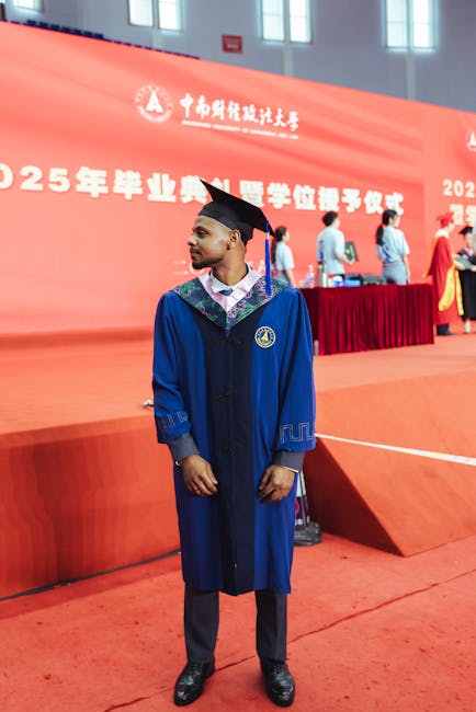 Young male graduate in blue academic gown during 2025 graduation ceremony indoors.
