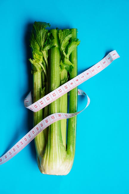 Vertical shot of fresh celery stalks wrapped in a measuring tape on a vibrant blue background.