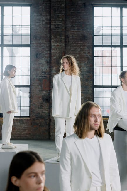 Young adults posing in white suits against industrial windows indoors, showcasing modern fashion.