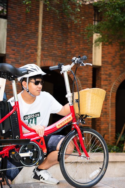 Man with red folding bike wearing helmet and sunglasses in urban setting.