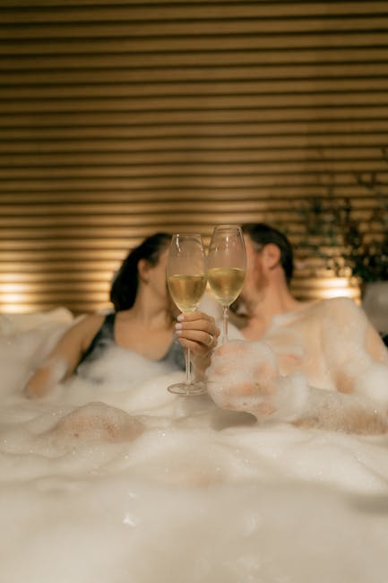 Couple enjoying a romantic moment with champagne in a frothy bubble bath indoors.