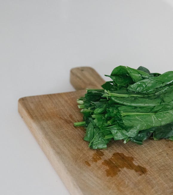 A fresh bundle of spinach resting on a wooden chopping board in kitchen lighting.