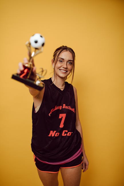 Smiling female athlete proudly holding a trophy in front of a vibrant yellow backdrop.