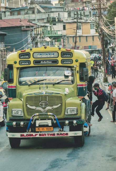 A vibrant commuter bus on a bustling street with people hanging on for a ride.