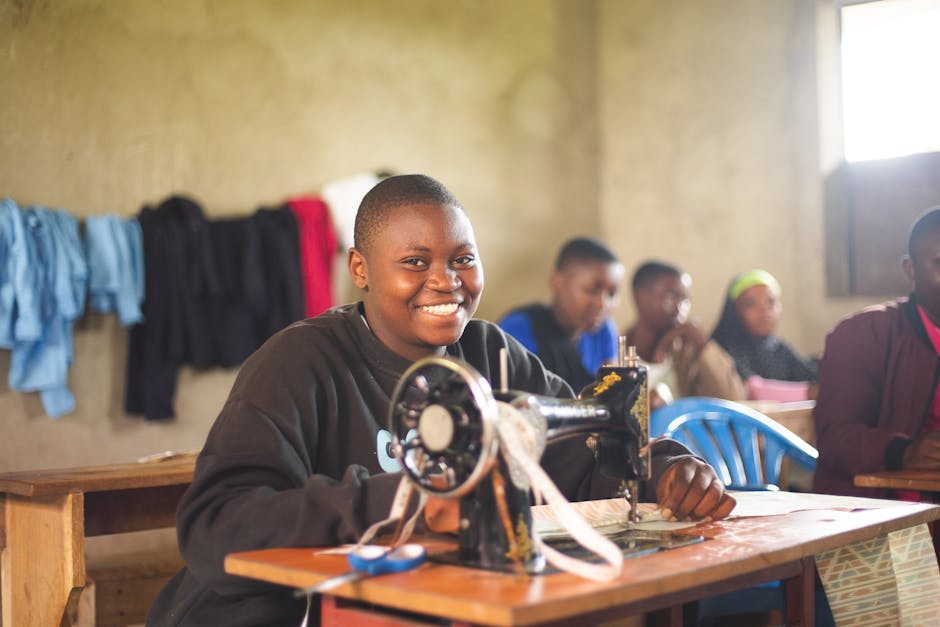 Happy student in Uganda using sewing machine in class, highlighting education.