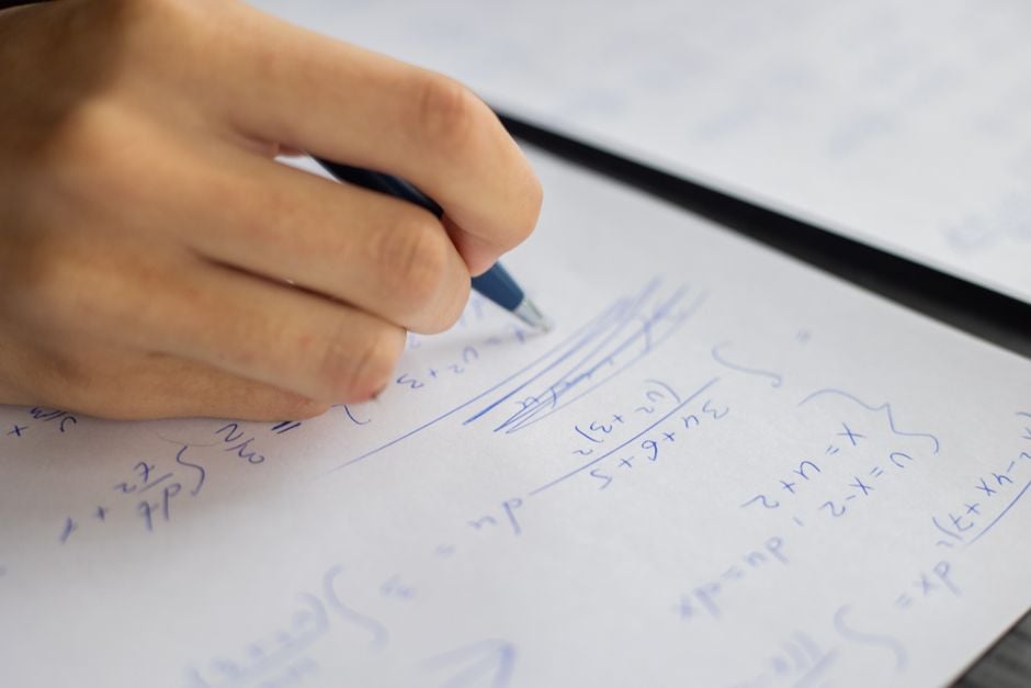 close-up hand solving math equations on paper with laptop and code