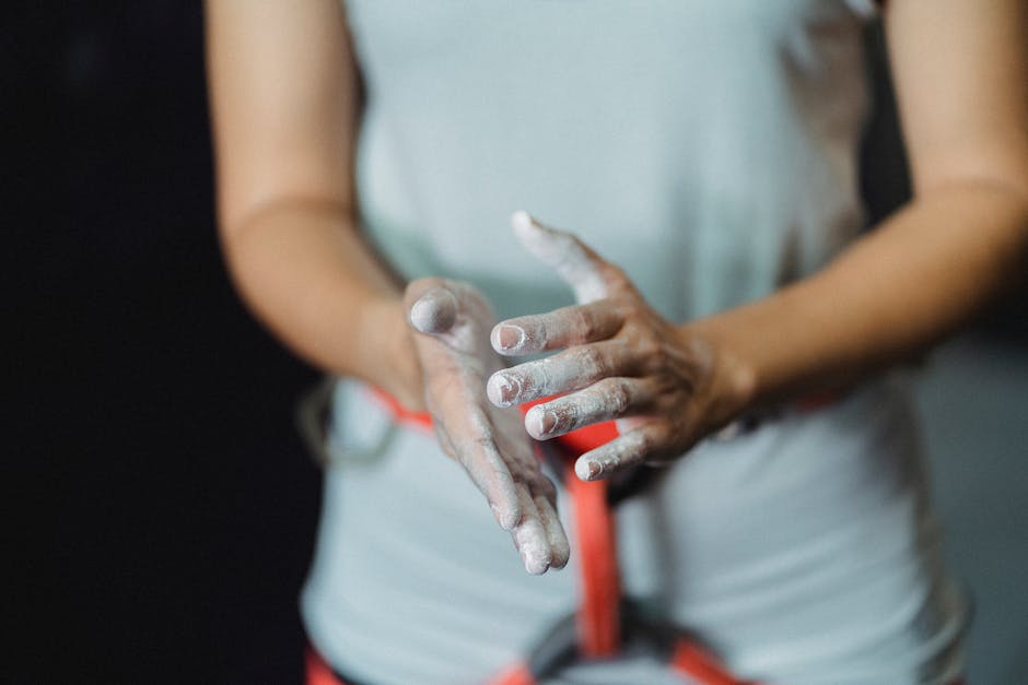 A female climber prepares by applying chalk to her hands before a climb indoors.