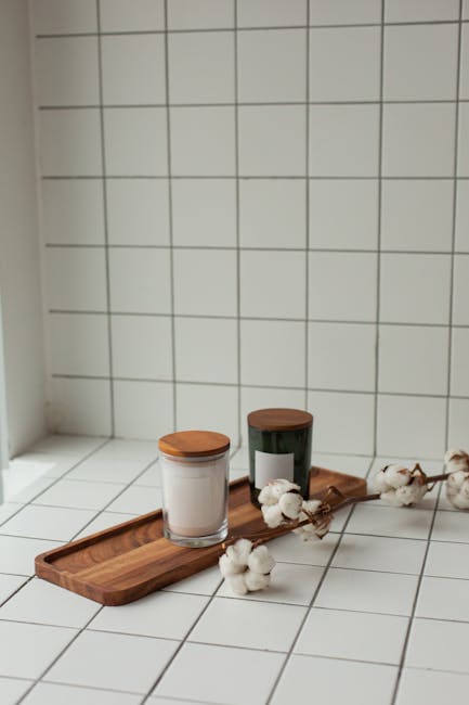 Stylish scented candles and cotton branches on white tiles, ideal for cozy home decor.