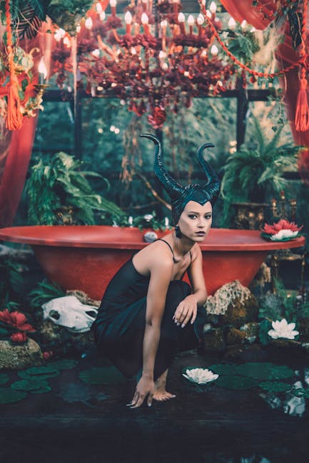 Woman in mystical forest with antler headpiece by a red bathtub, surrounded by plants.