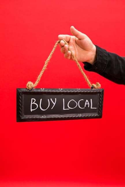 Person holding a 'Buy Local' sign suspended on ropes, promoting local business.