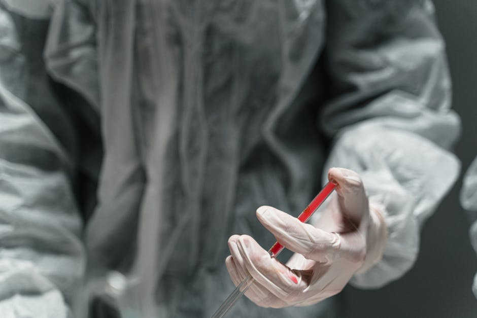 Scientist in protective gear handling a syringe in a laboratory setting.