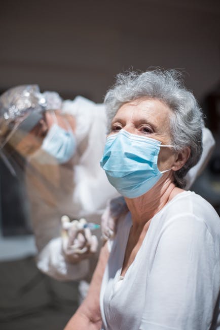 A senior woman receives a vaccine from a medical professional in a healthcare setting.