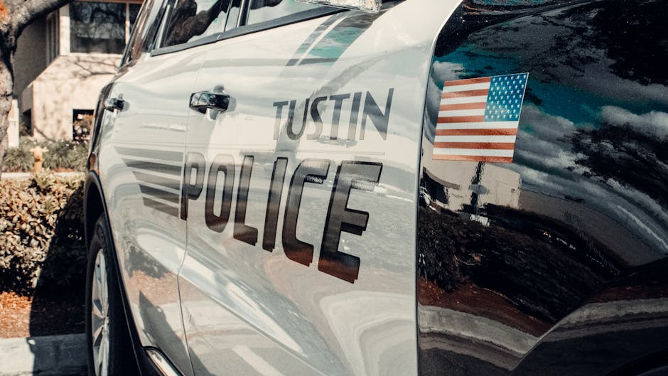 Reflective image of a Tustin police car parked outdoors with an American flag emblem.