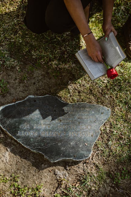 A woman kneels at a gravestone, reading a book with a red rose, symbolizing remembrance.