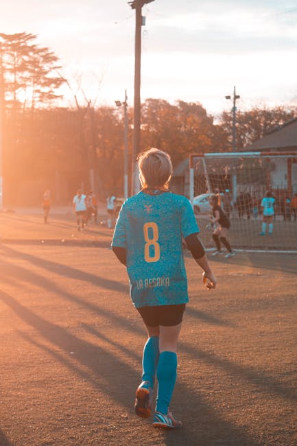 Teen girl in soccer attire on field at sunset, showcasing athletic skill and teamwork.