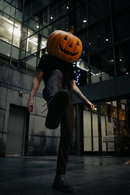 A man with a carved pumpkin head strolls through a modern urban area in Chicago at night.