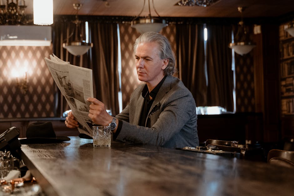 A senior man in a gray suit reads a newspaper at a bar, setting a classic, contemplative mood.