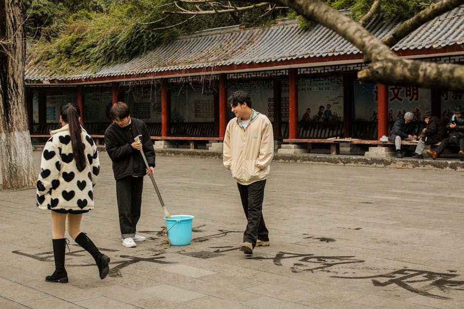People practicing calligraphy outdoors using a giant brush, set in a traditional Chinese setting.
