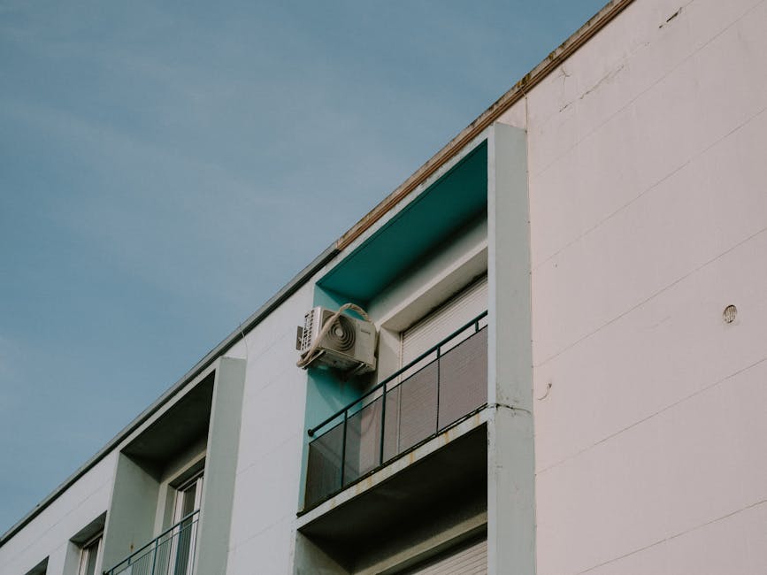 A low angle view of a modern apartment building featuring a balcony and air conditioner unit.