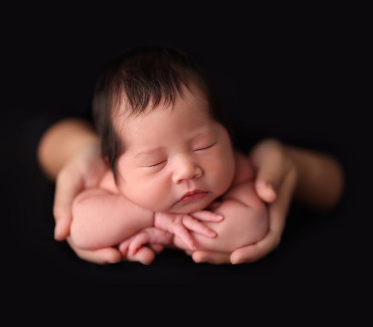Close-up of an adorable Asian newborn baby sleeping peacefully cradled in loving hands.