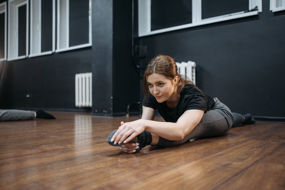 A woman performs a stretch on a wooden floor in a dance studio, showcasing flexibility and fitness.