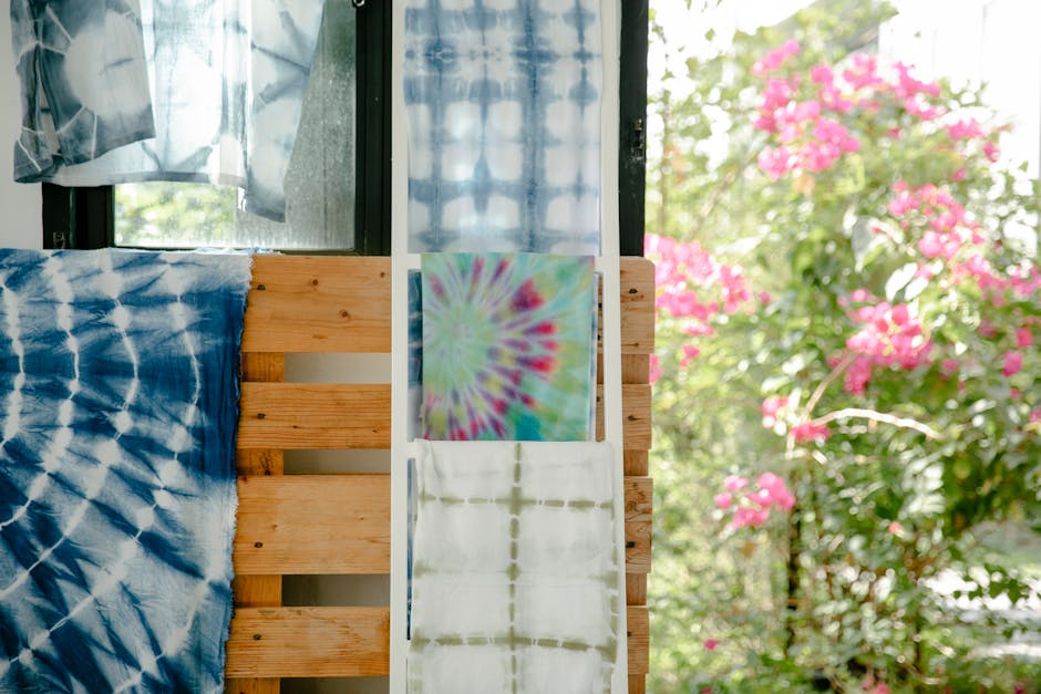 Colorful tie-dye fabrics displayed in a bright, sunlit workshop with blooming flowers outside.