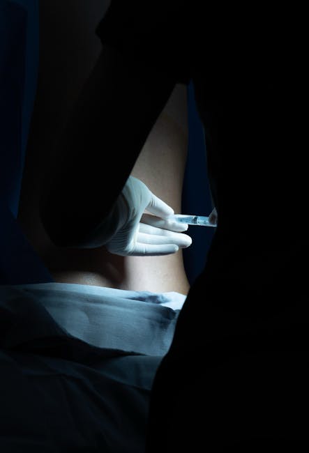 A healthcare worker in gloves administering a syringe injection to a patient in a dimly lit setting.