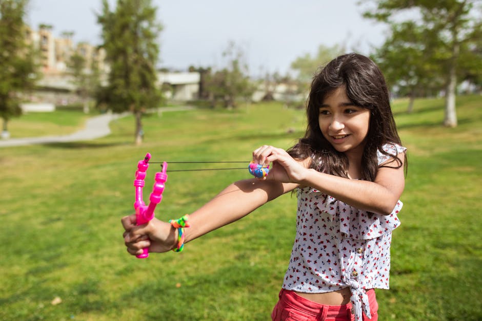 A cheerful girl enjoying a playful moment with a colorful toy bow in a sunny park.