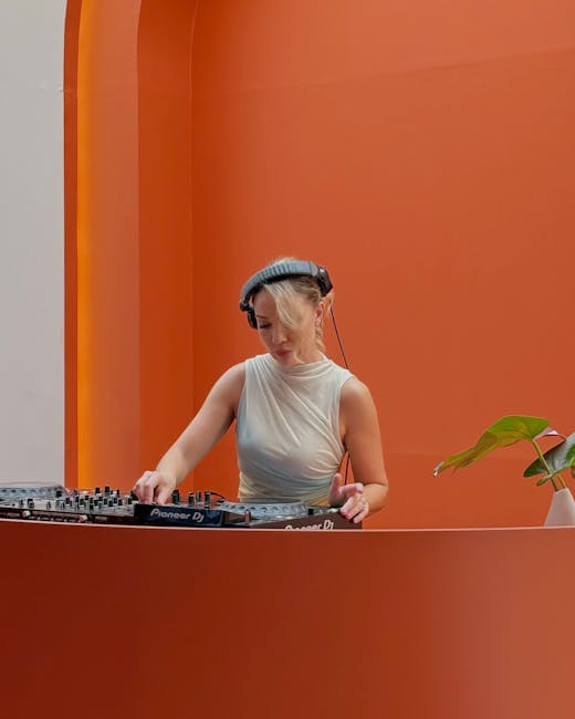 A DJ in a white top mixes music against a vibrant orange backdrop in Dubai, UAE.