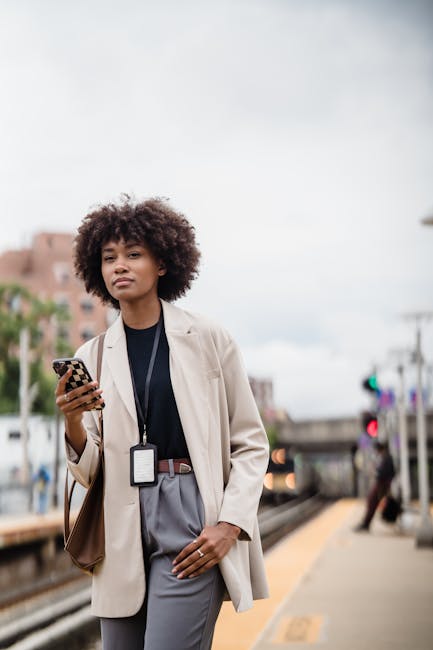 Young woman with curly hair in jacket using phone at a train station.