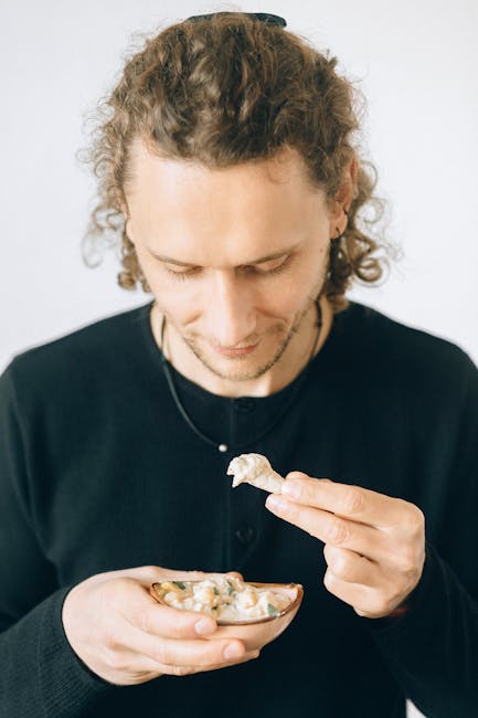 A man holding and enjoying a bowl of traditional Middle Eastern falafel dip with pita bread.